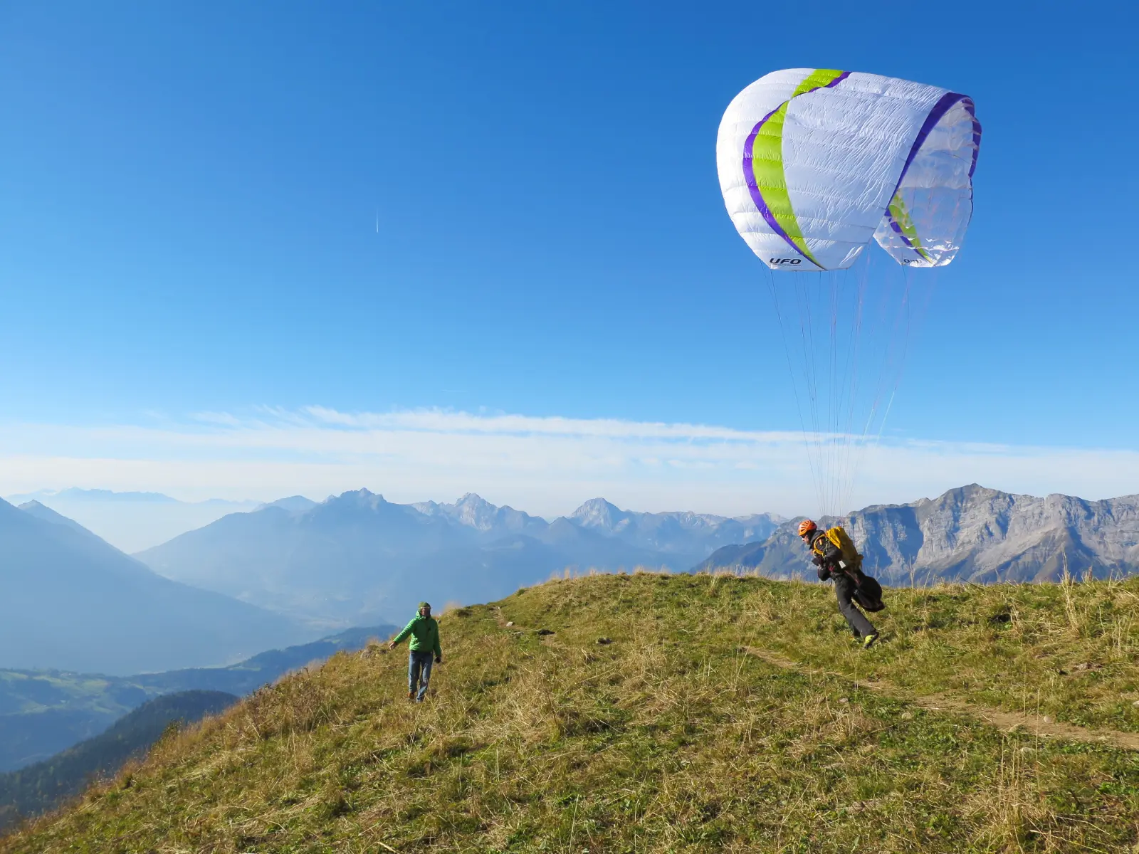 Un élève parapentiste commence son décollage sous l'attention soutenu de son moniteur lors d'un stage d'initiation de parapente. Le parapente est au dessus de la tête de l'élève, il court pour décoller