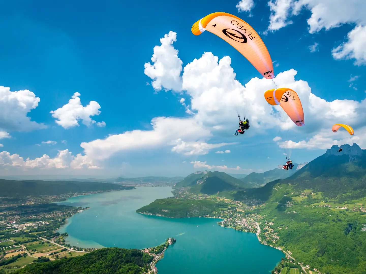 Deux parapentes oranges volent sous les nuages cumulus blancs et au dessus du lac bleu