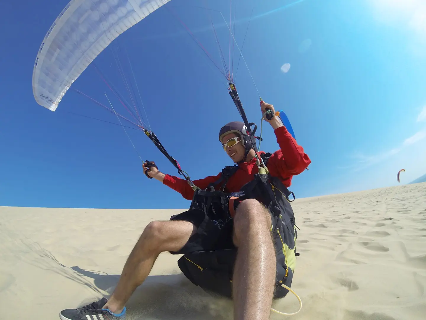 A paraglider controls his wing on the ground on the dune