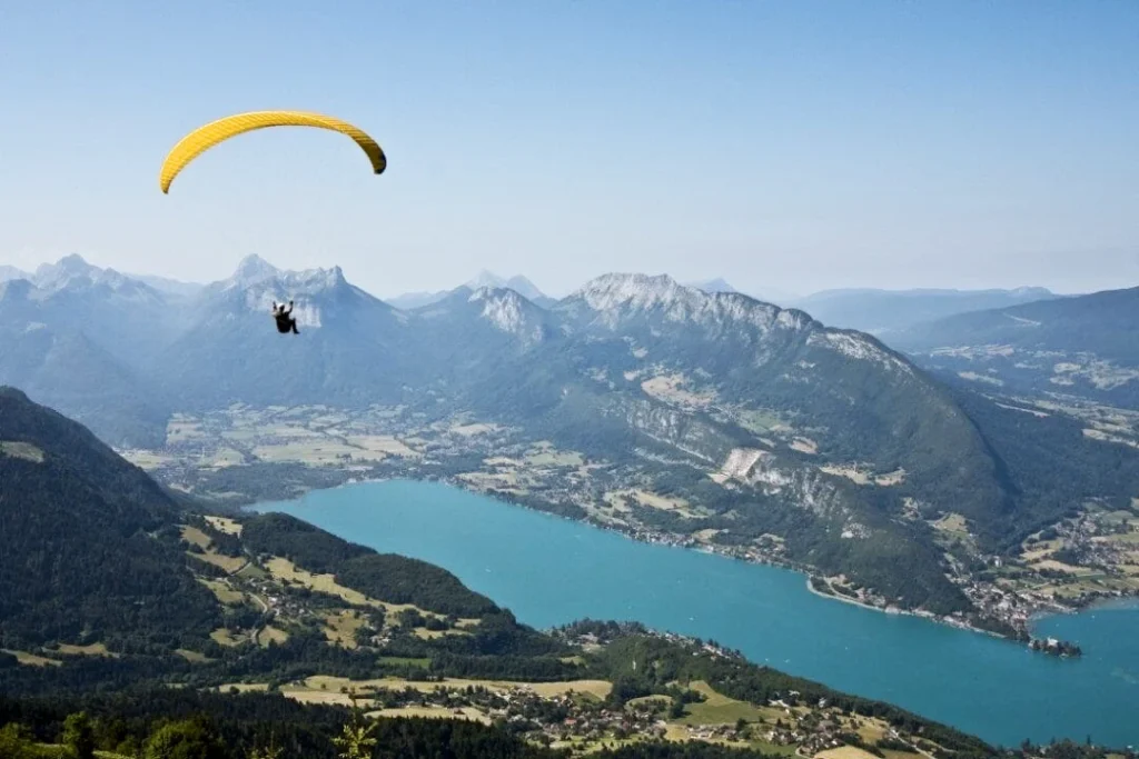 Un parapente jaune avec son pilote volent au dessus du lac Annecy