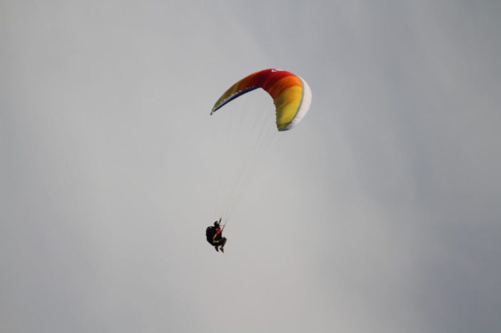 A paragliding pilot stalls his wing on purpose, the paraglider holds back behind the pilot and is croissant shaped