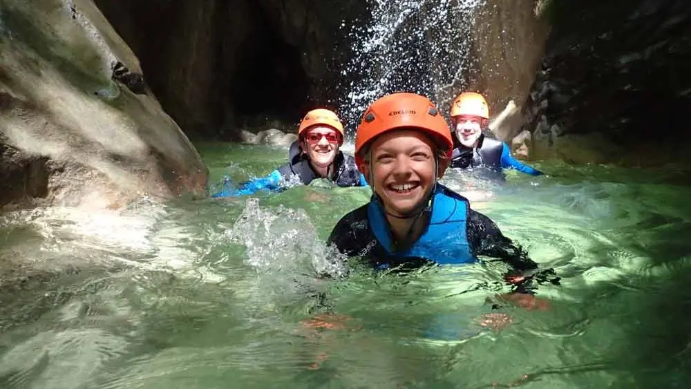 Une petite fille qui porte un casque est dans l'eau d'une cascade lors d'une sortie en Canyoning