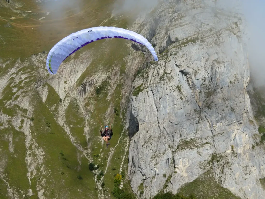 Un parapentiste dessous son parapente monosurface vole à proximité d'une falaise de pierre