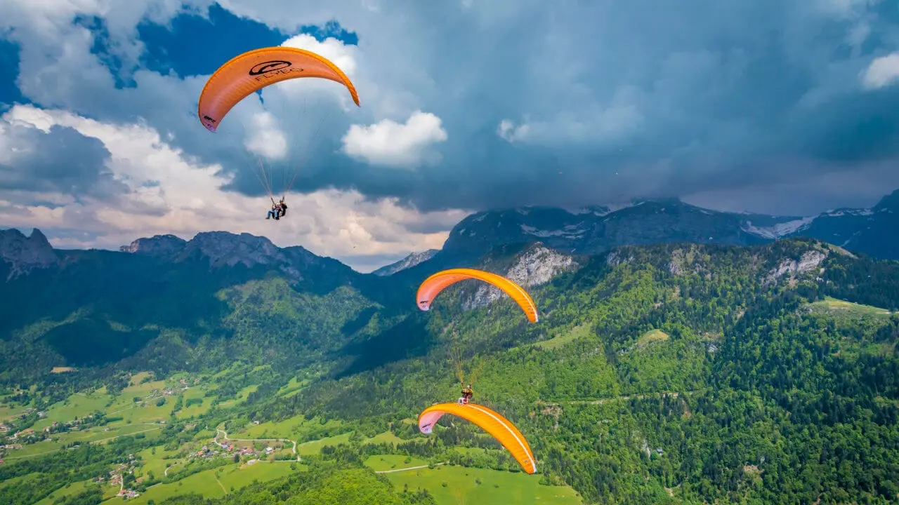 Deux parapentes oranges Flyeo volent au dessus du lac avec les montagnes vertes en arrière plan