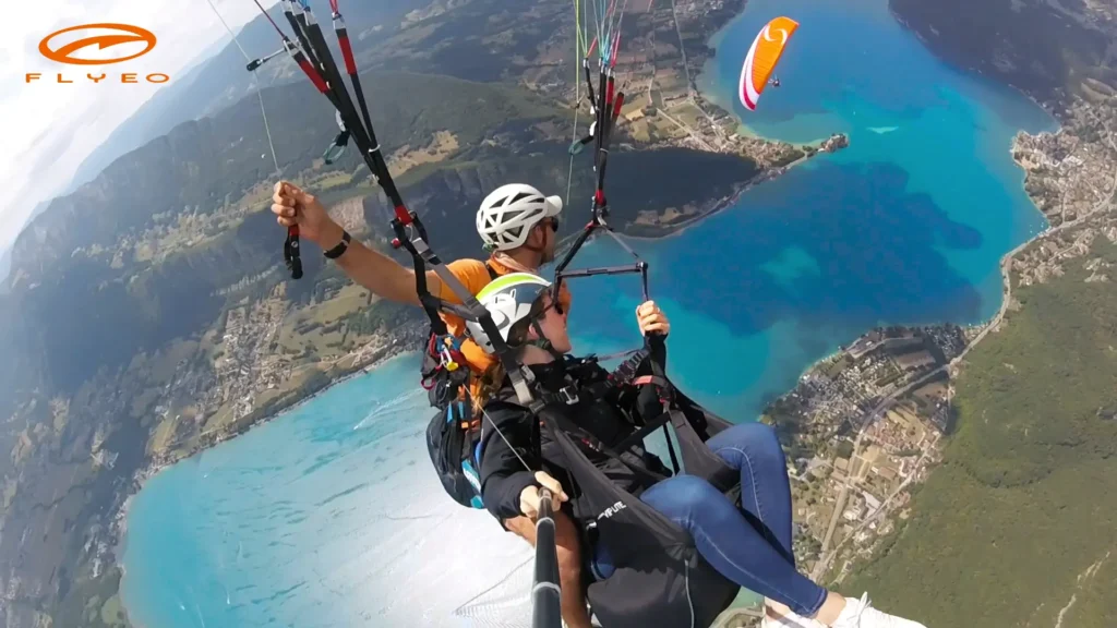 Un pilote et sa passagère sont engagés dans une spirale synchronisée avec un autre parapente que l'on voit en arrière plan